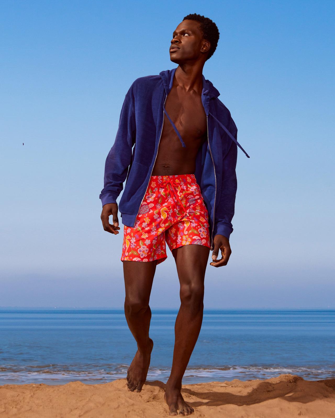 A man in a blue jacket and shorts on the beach.