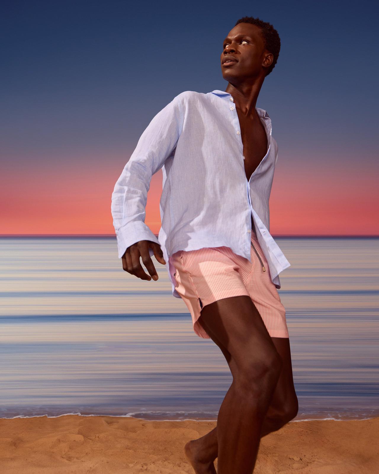 A man in a white shirt and pink shorts standing on a beach.