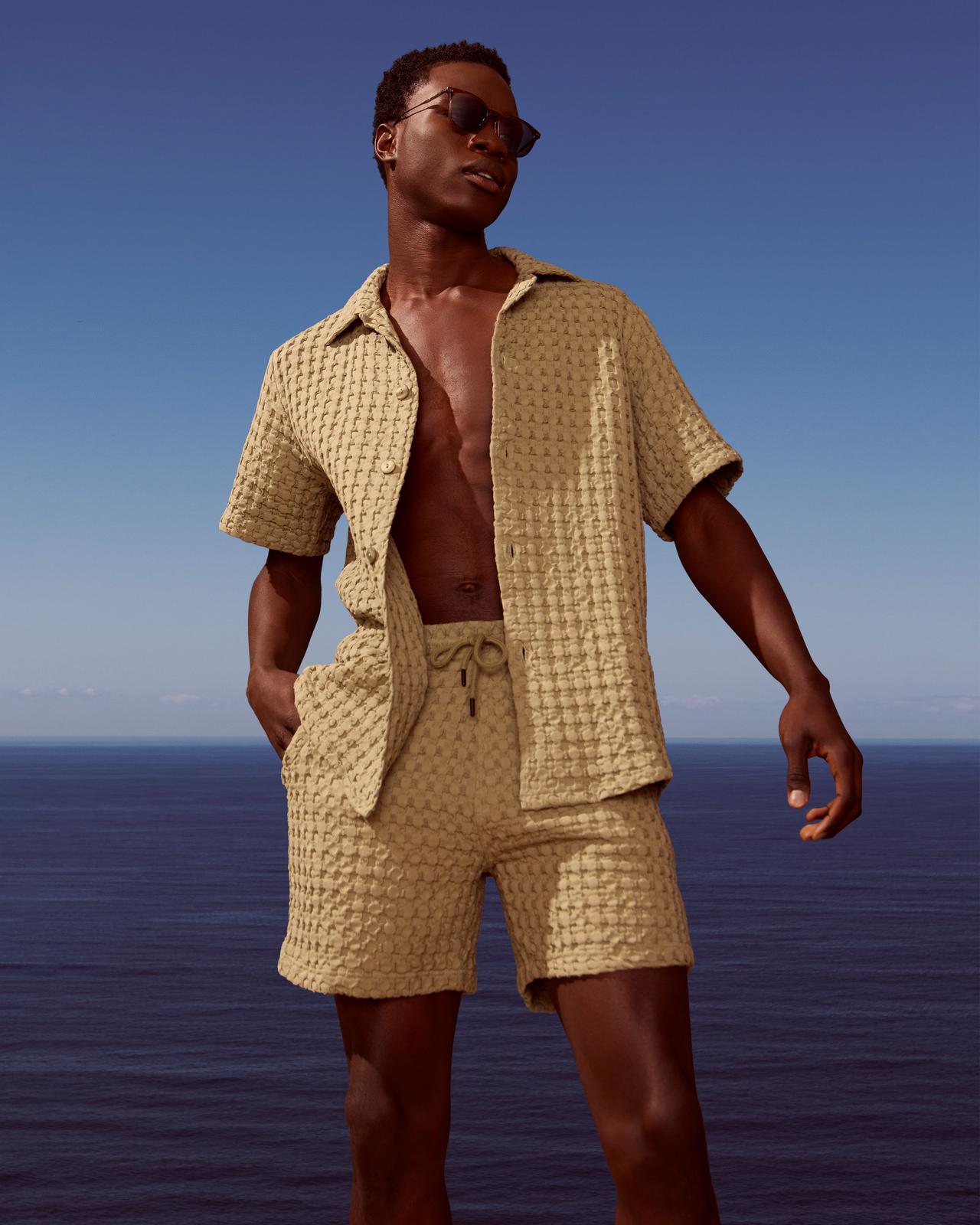 A man in a tan shirt and shorts standing on a beach.