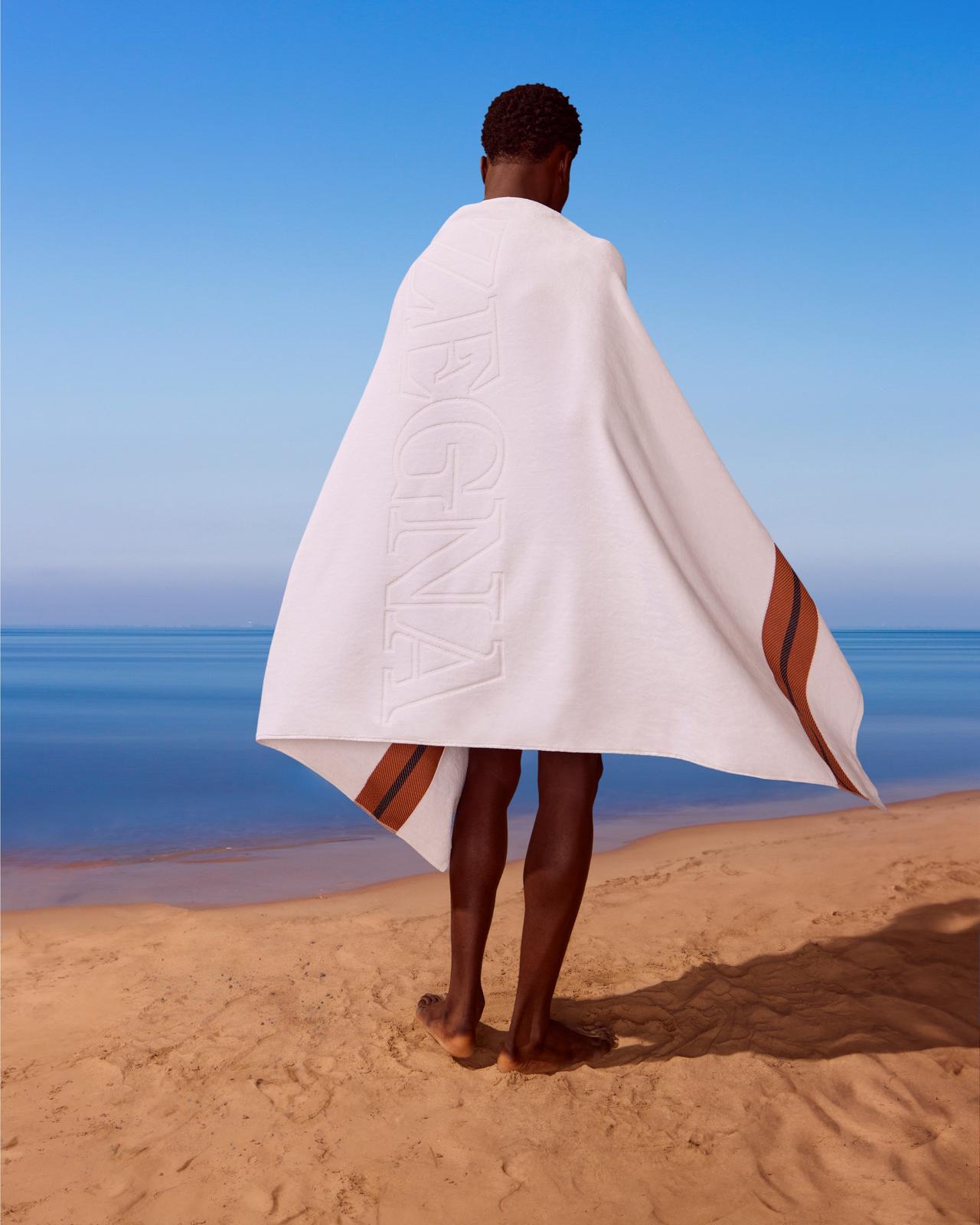 A man standing on the beach wearing a Zegna towel.