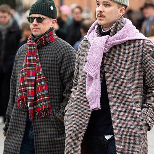 Two men wearing coats and scarves walking down a street