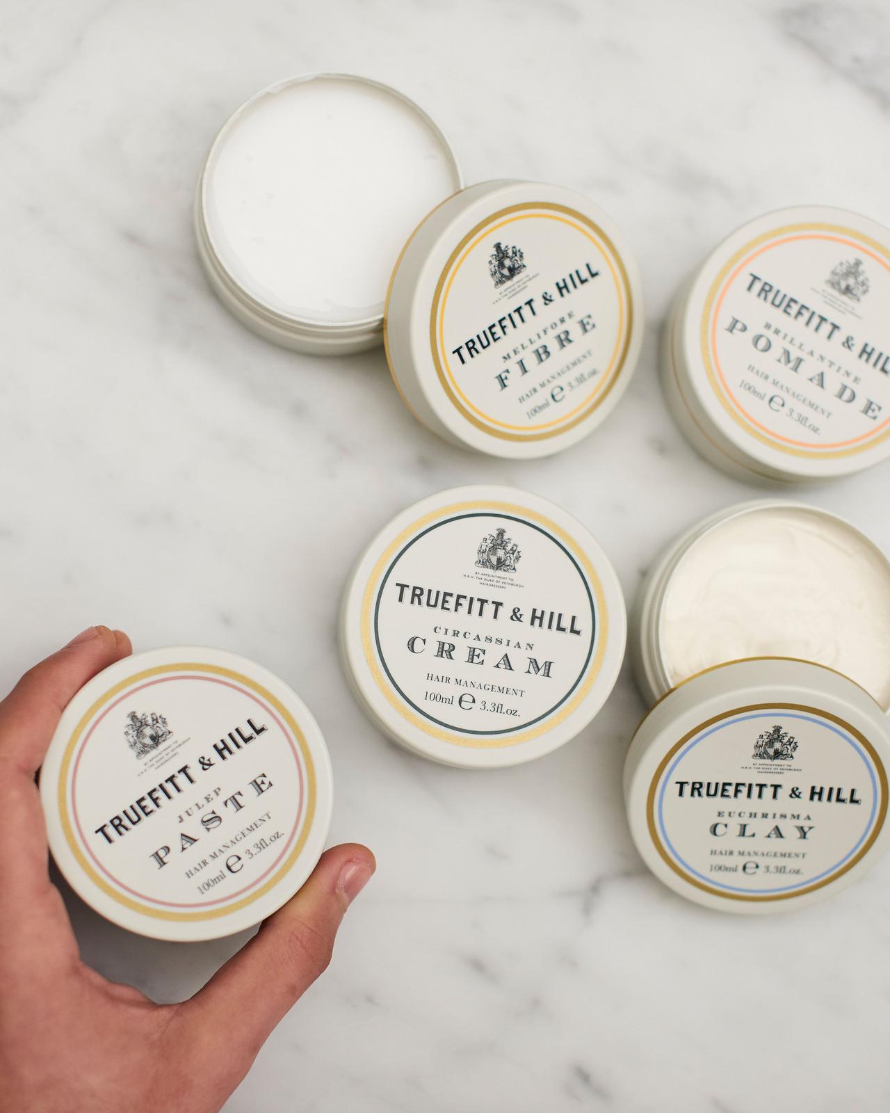 main masculine tenant un récipient de produit de toilettage deux contenants de produits de soins ouverts et deux produits de soins fermés présentés sur un comptoir en marbre