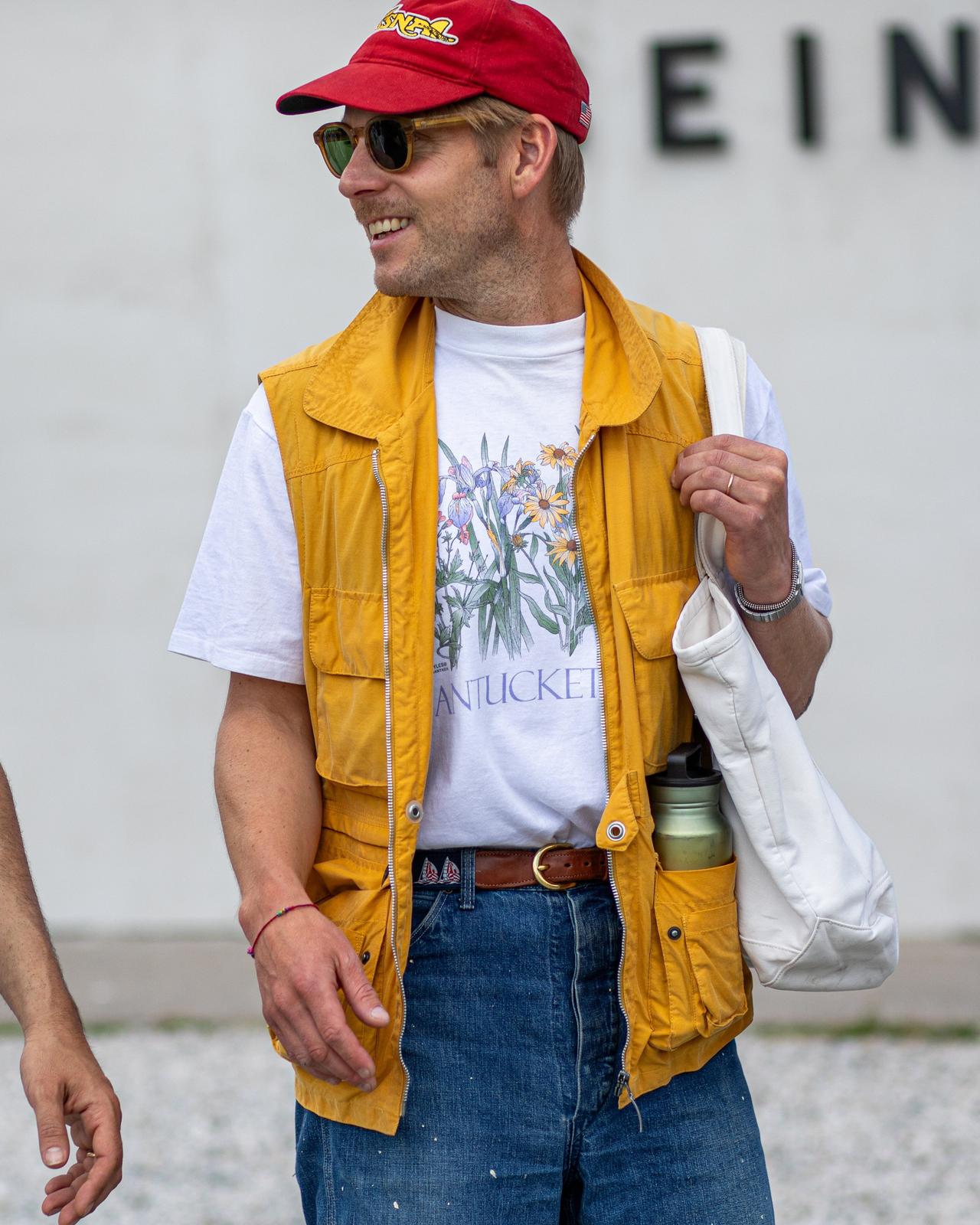 a man in a yellow vest and a red shirt walking down the street