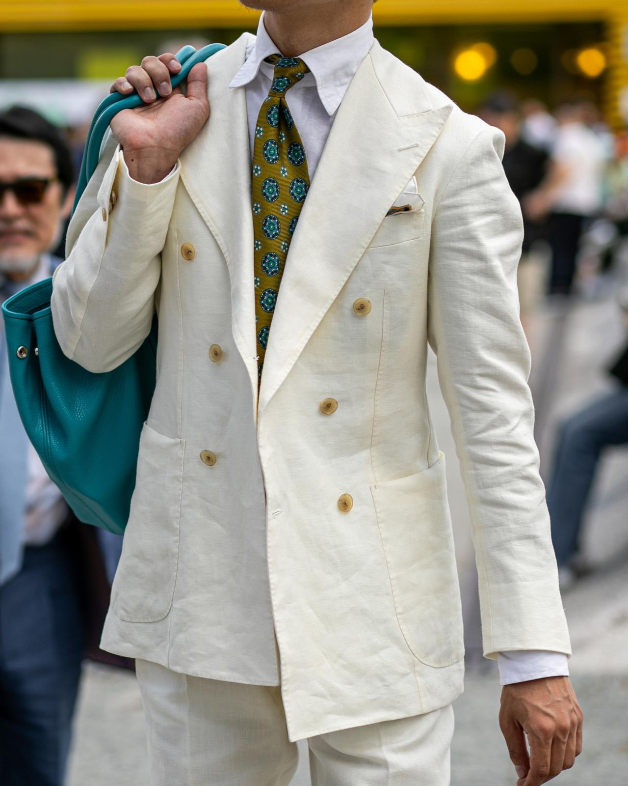 a man in a white suit and tie holding a blue bag