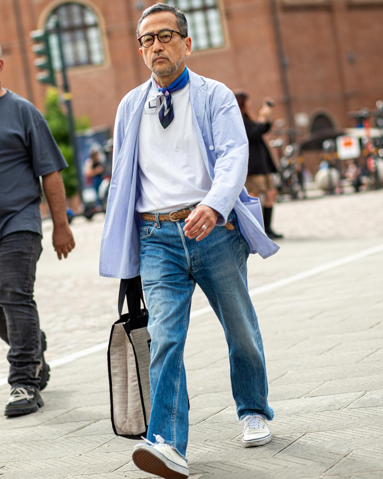 man walking in the street wearing glasses, neck scarf, t-shirt, jeans with belt and overshirt