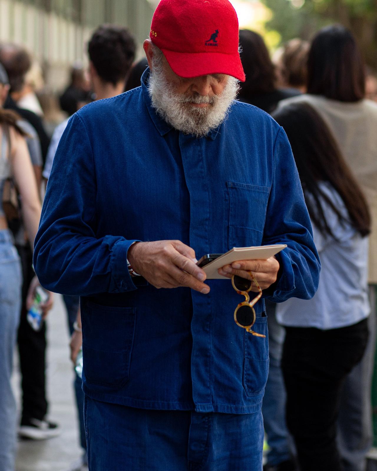 male outside looking down holding notepad and cellphone wearing baseball cap, sport shirt, and jeans