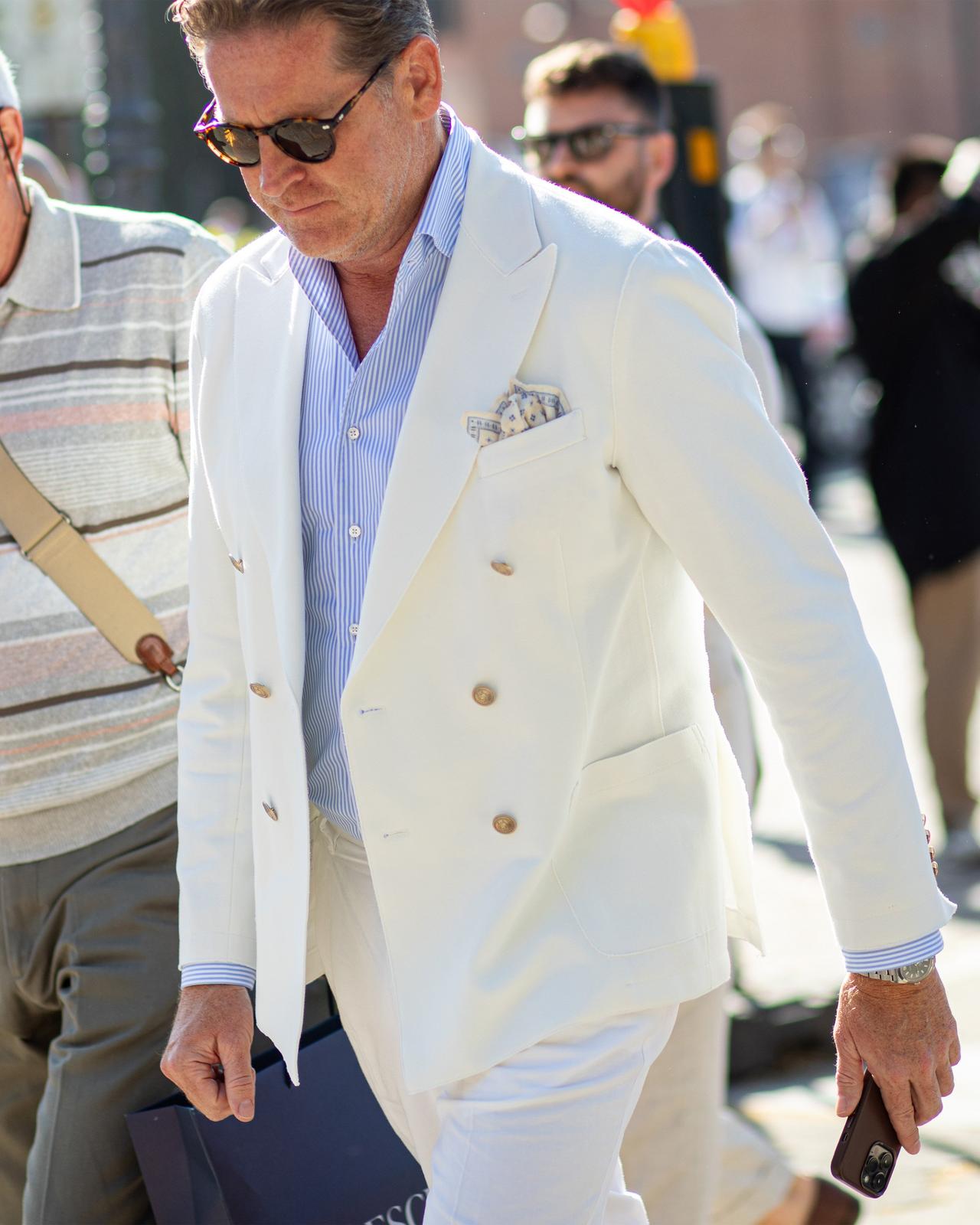 un homme en costume blanc marchant dans une rue avec un téléphone portable