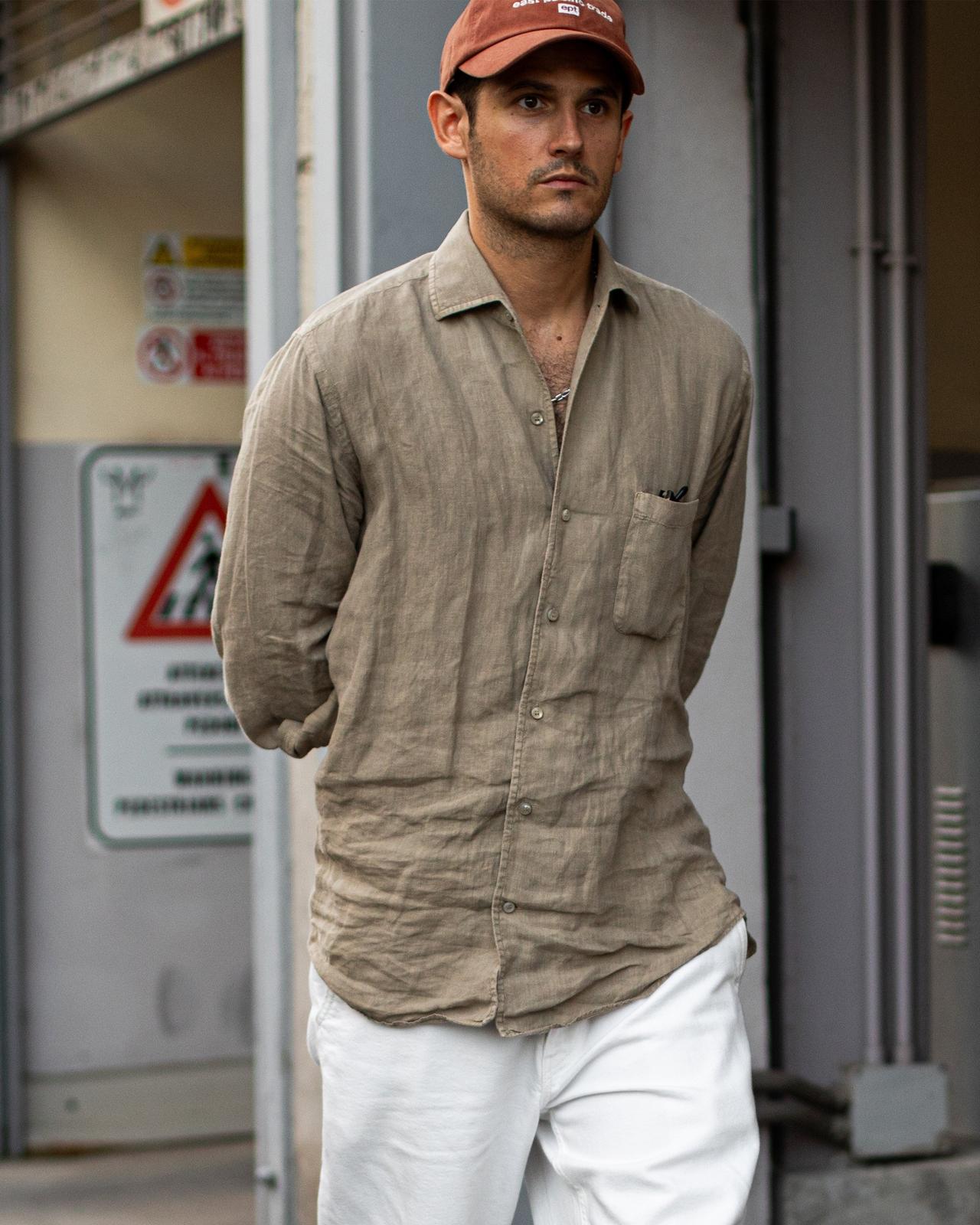 male walking outside with hands behind back wearing sport shirt, baseball cap and white jeans