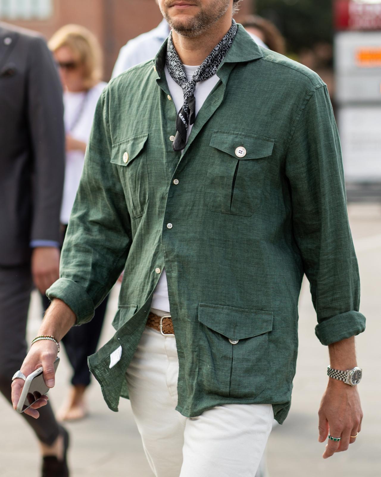 a man in a green shirt and white pants walking down a street