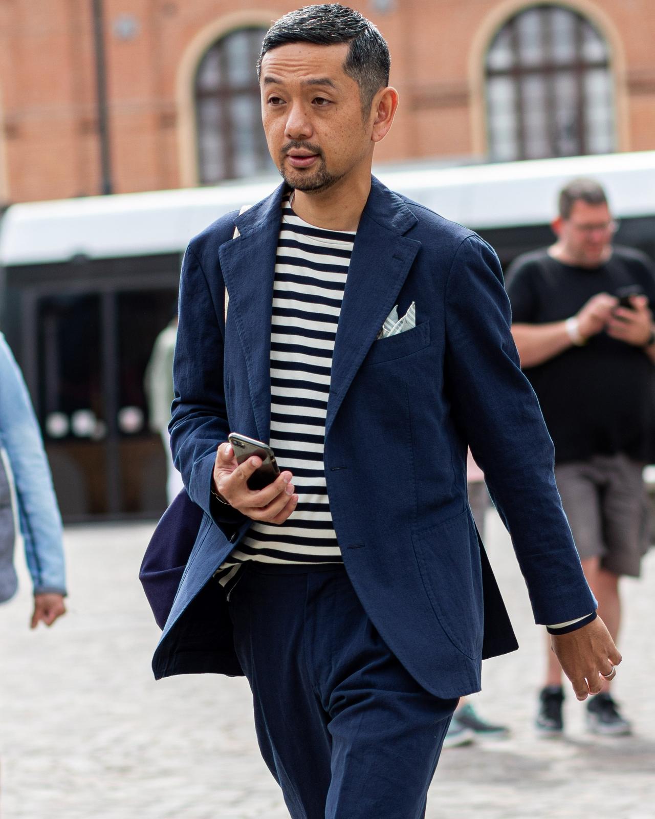 man wearing striped t-shirt and sport jacket holding cellphone walking in the street