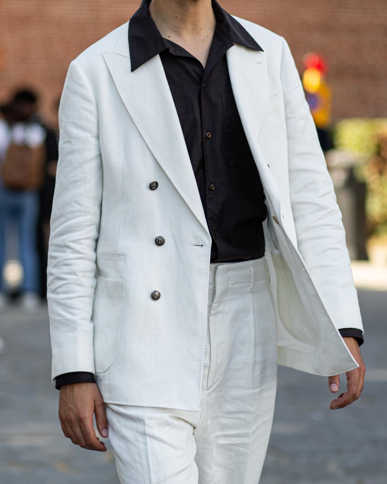 un homme en costume blanc et chemise noire marchant dans une rue