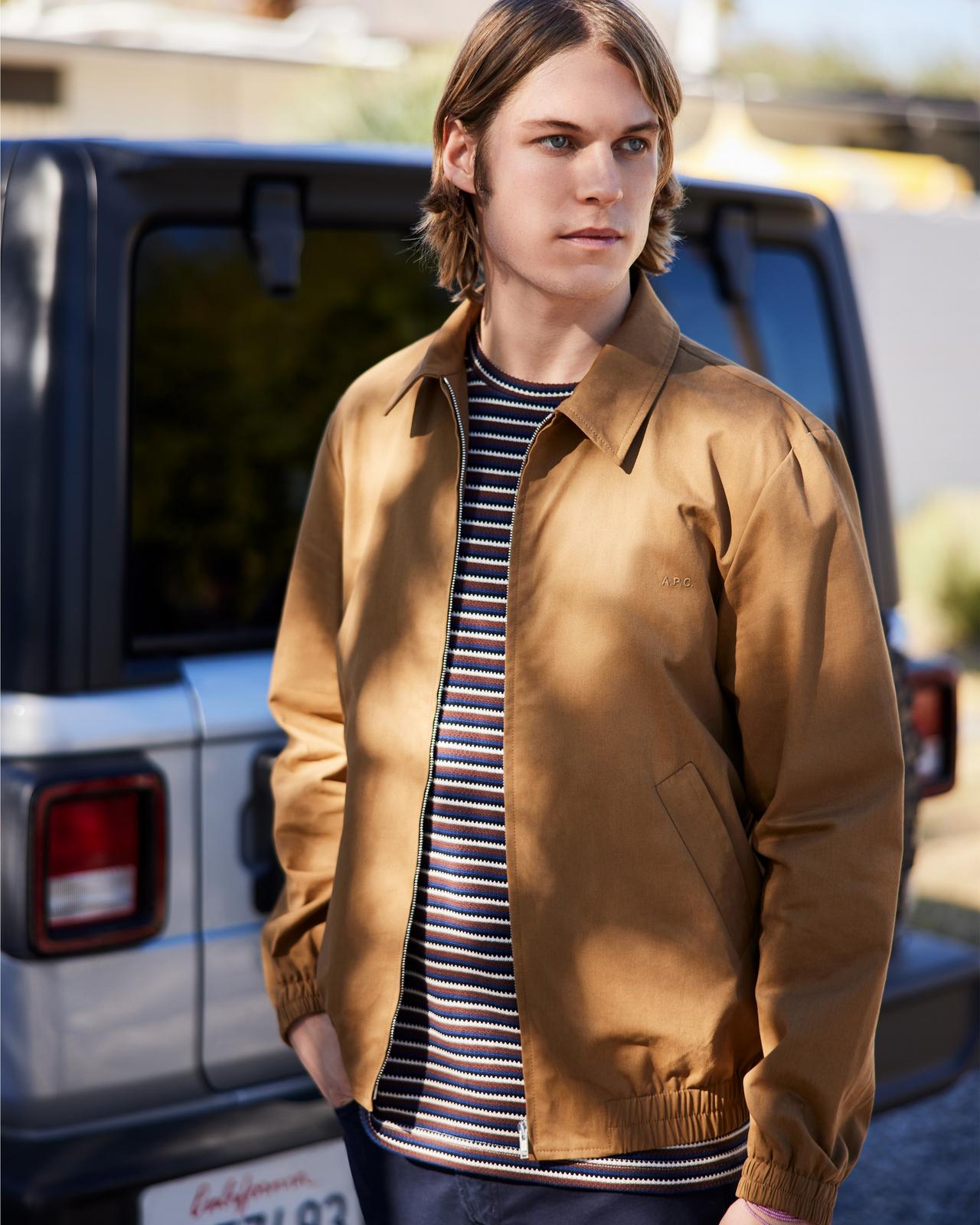 a man in a jacket and striped shirt standing next to a car