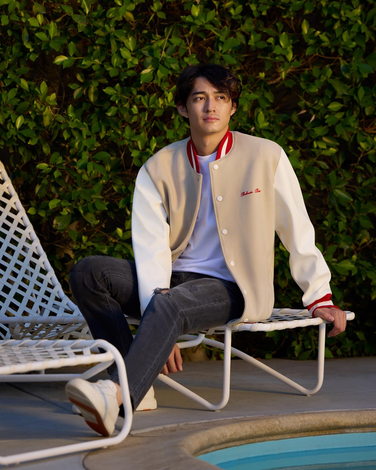 a man sitting on a pool chair wearing a balmain bomber