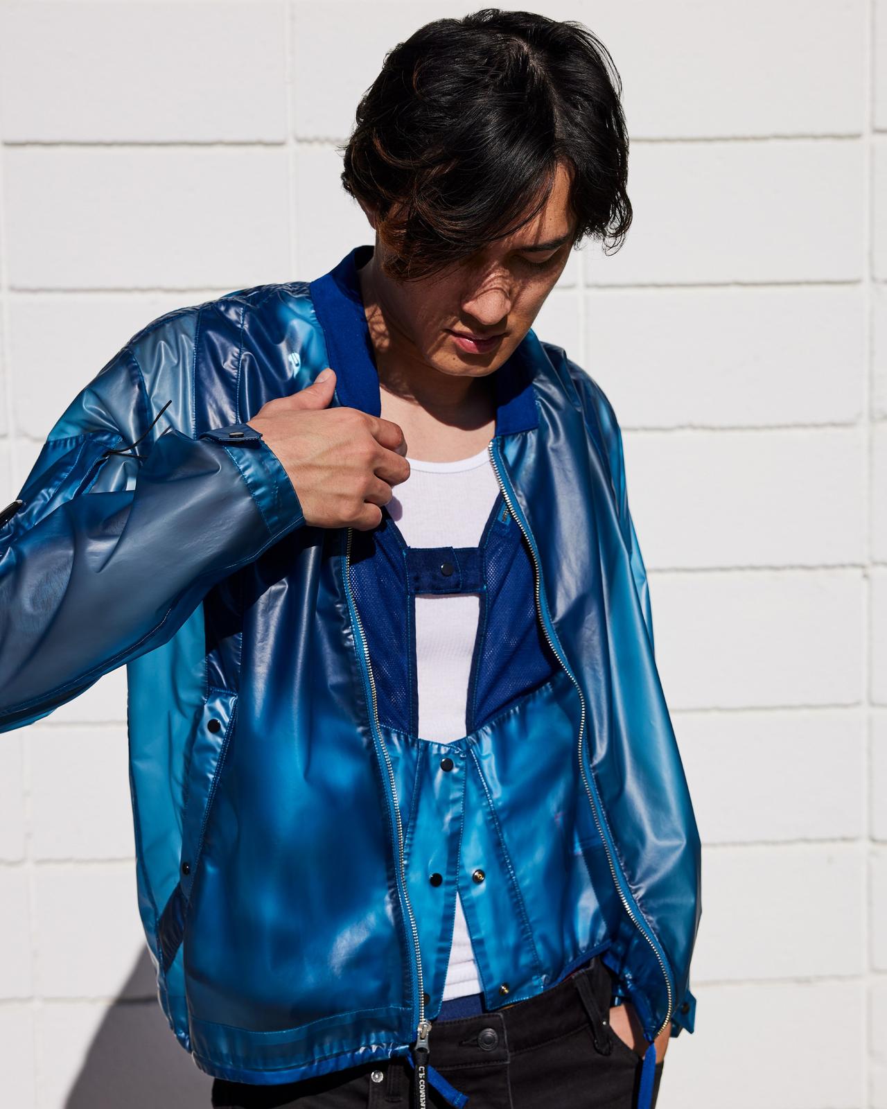 a man in a blue jacket standing next to a white wall