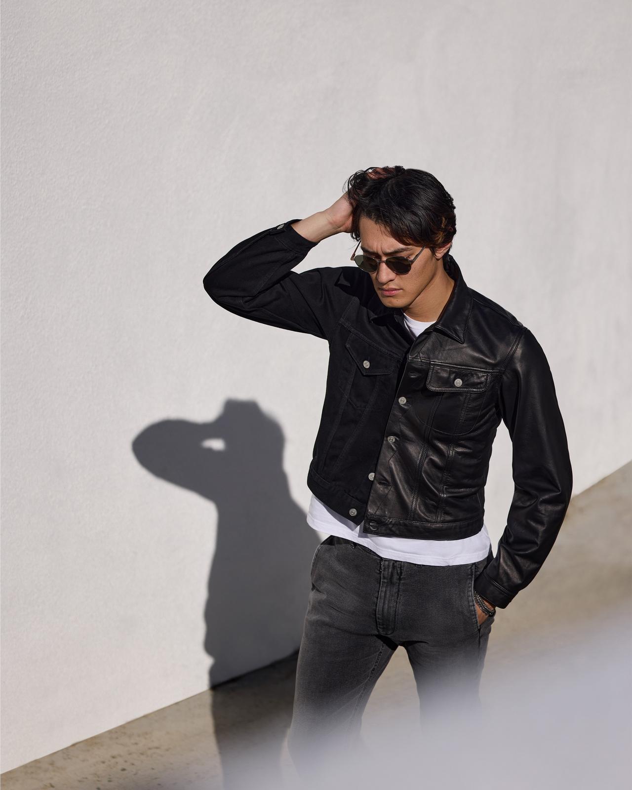 a man in a black jacket and jeans standing next to a wall