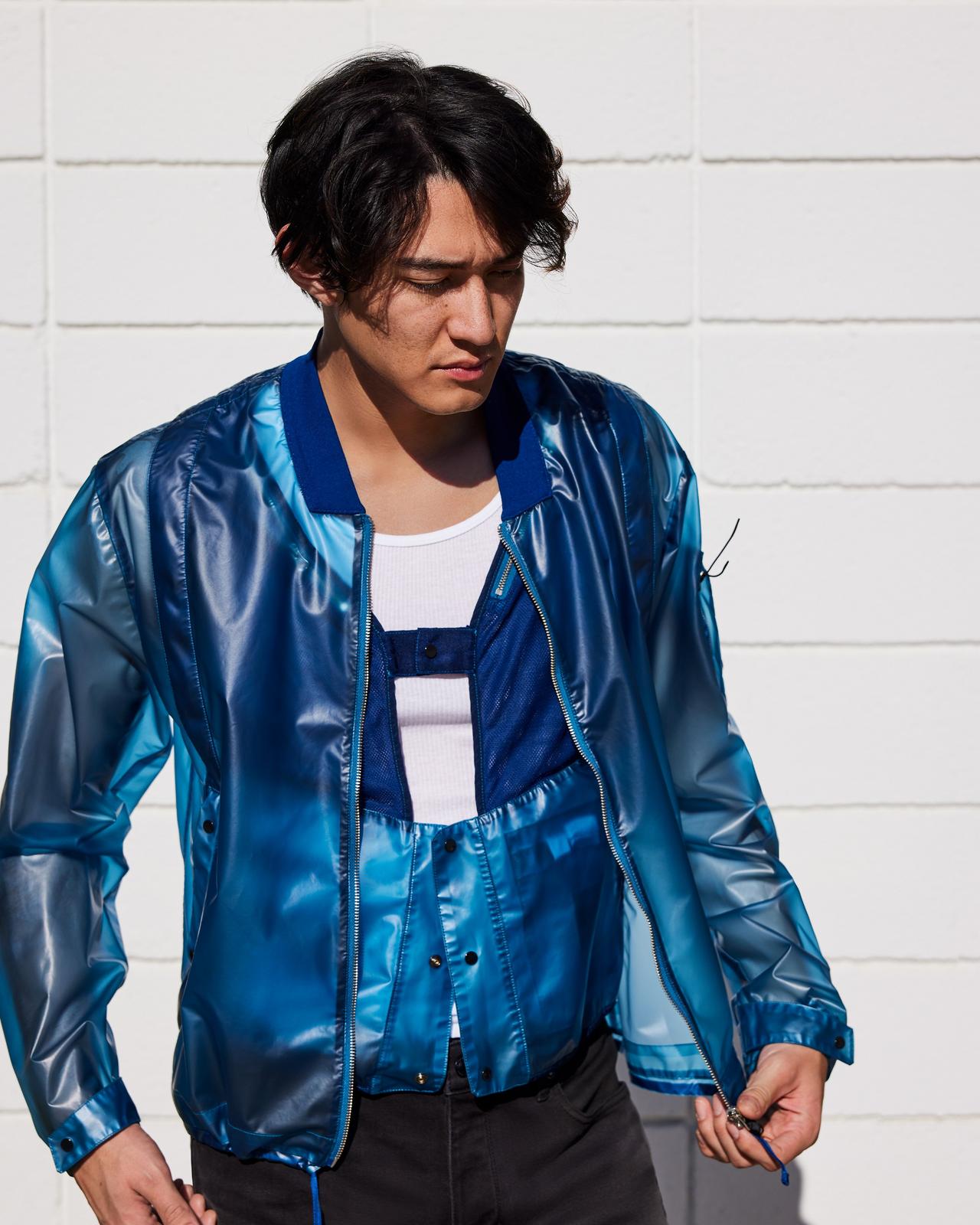 a man in a blue jacket and white shirt standing against a wall