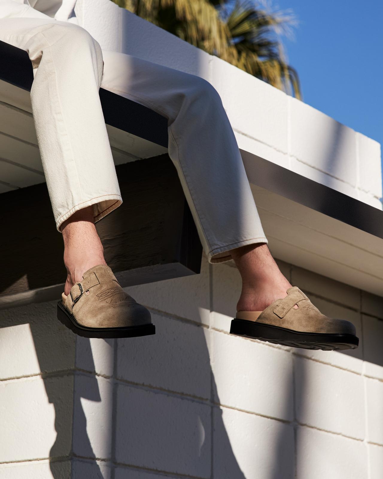 une personne assise sur un rebord en pantalon blanc, les pieds pendants