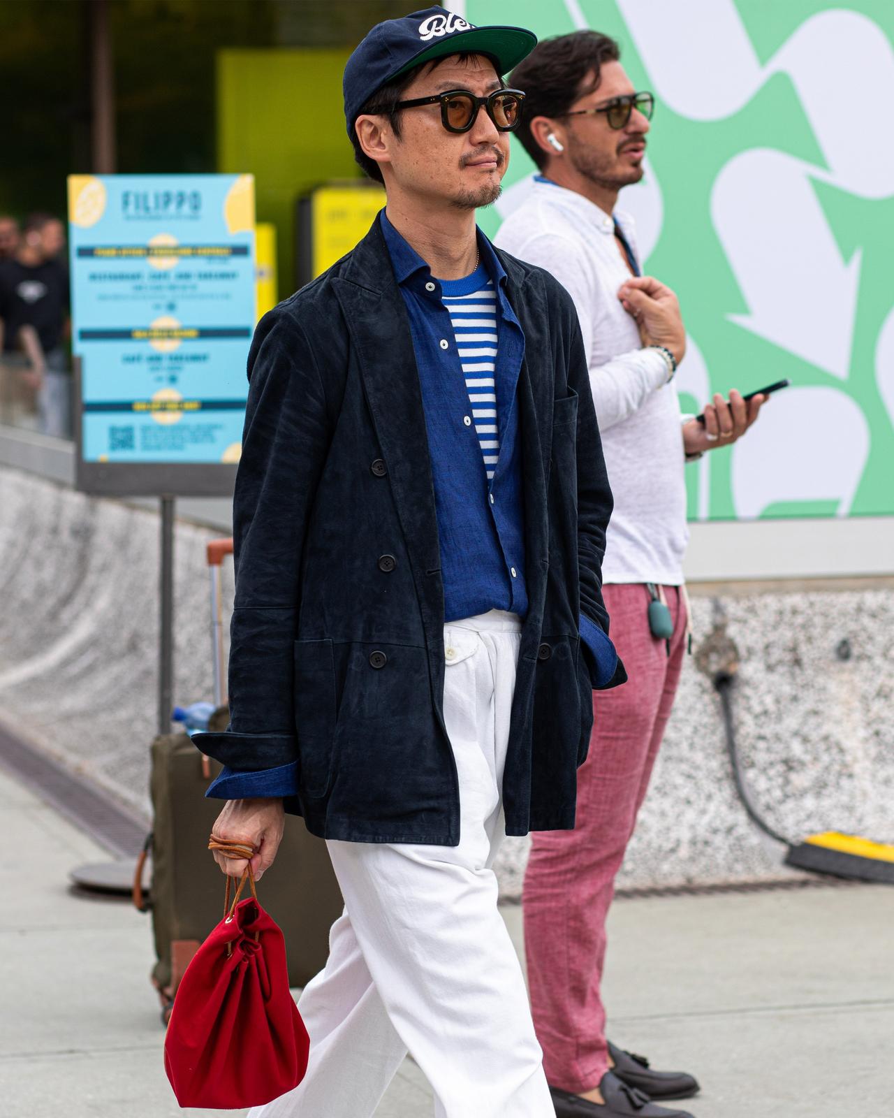 a man in a blue jacket and white pants walking down the street