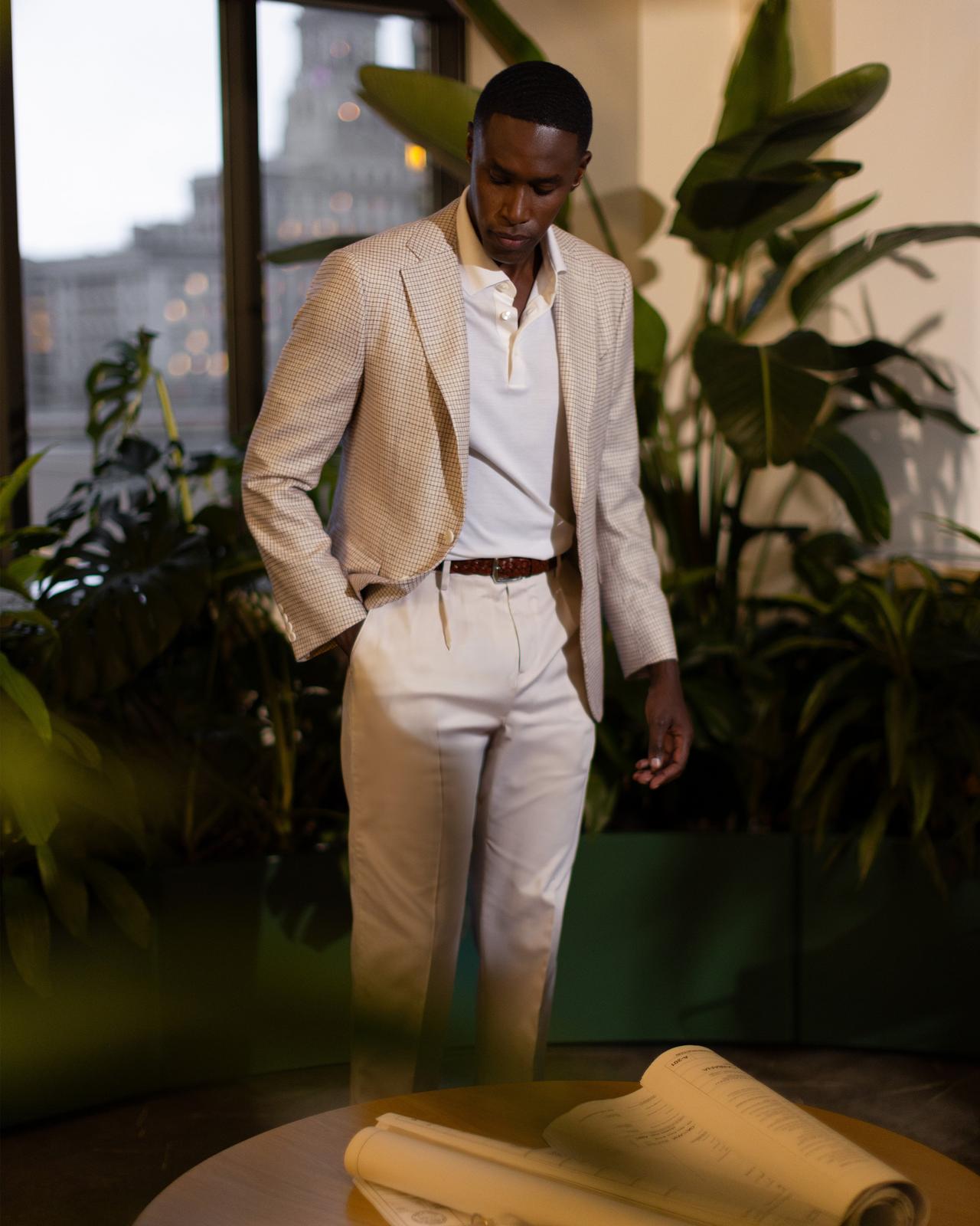 un homme en costume beige et polo blanc debout dans un jardin intérieur