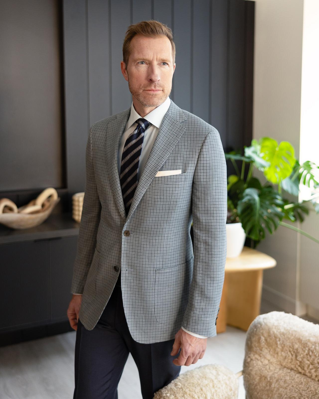 a male in a grey sport jacket and striped tie standing in an office