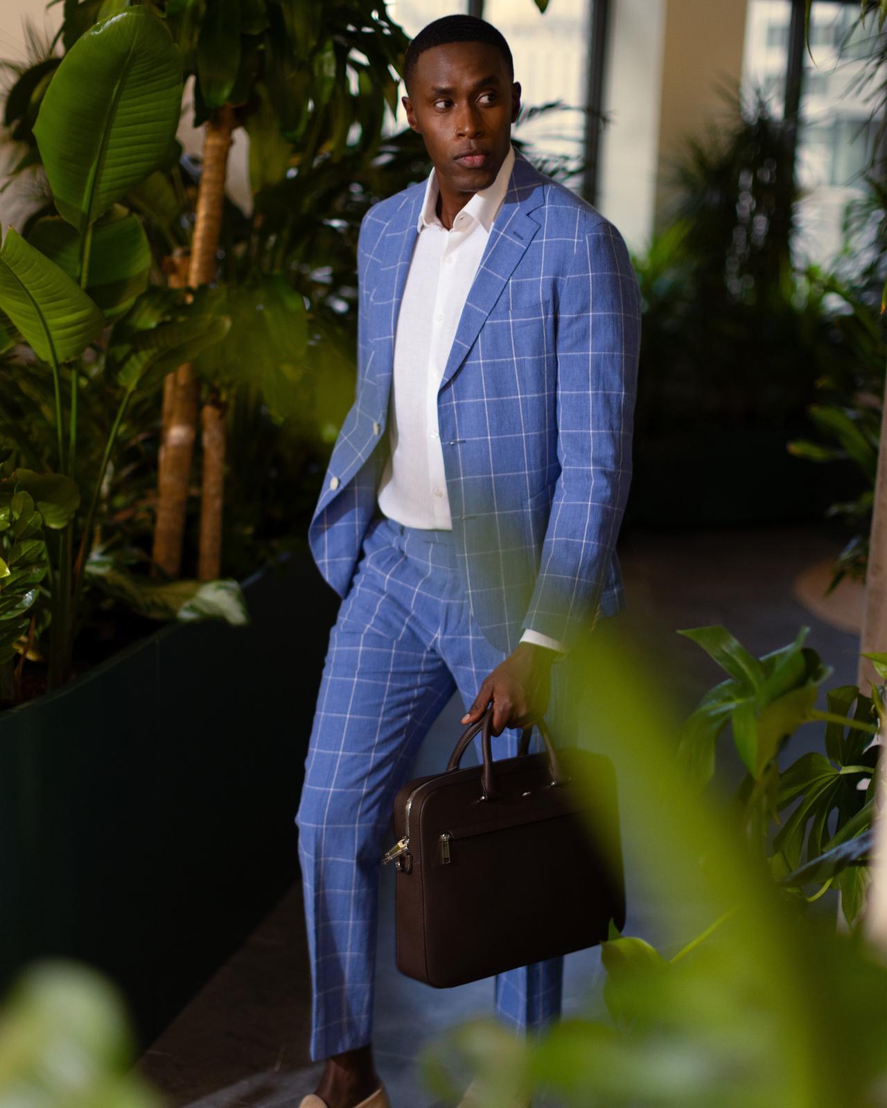a male in a blue checked suit holding a briefcase in an indoor garden