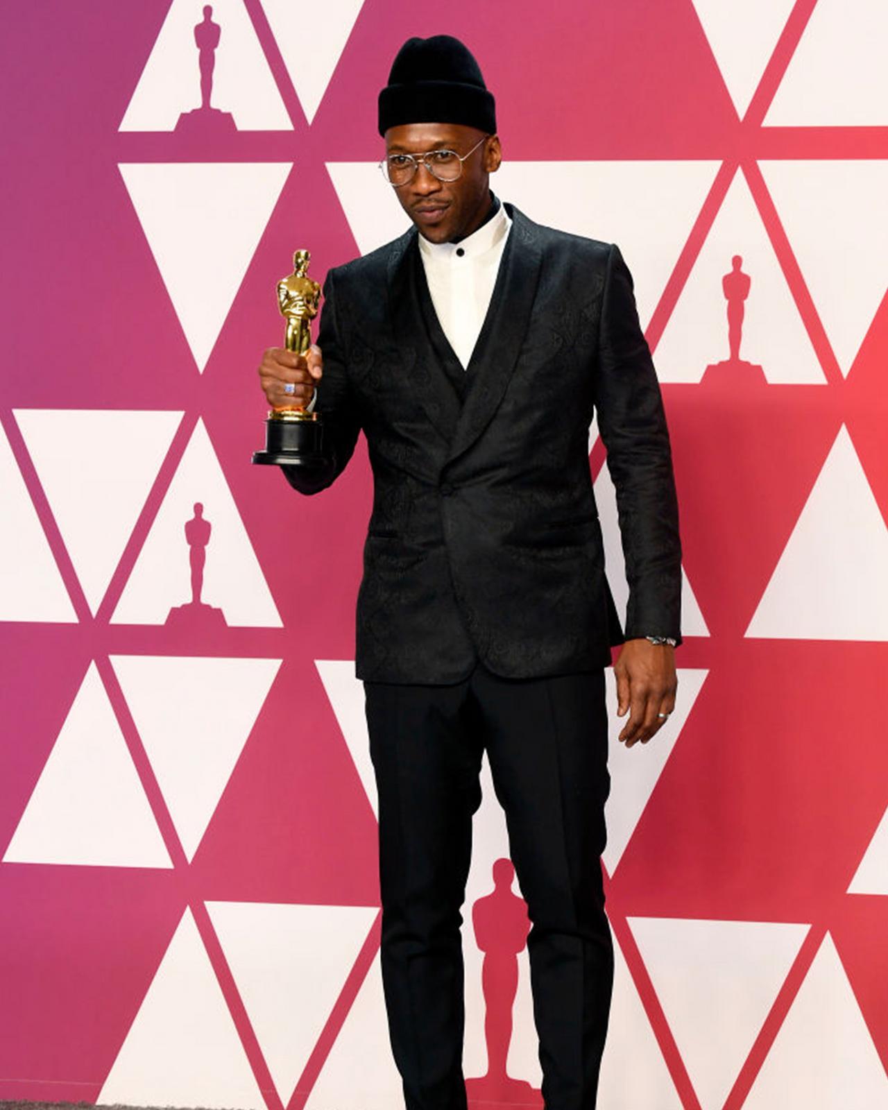 Mahershala Ali in a suit holding an oscar award