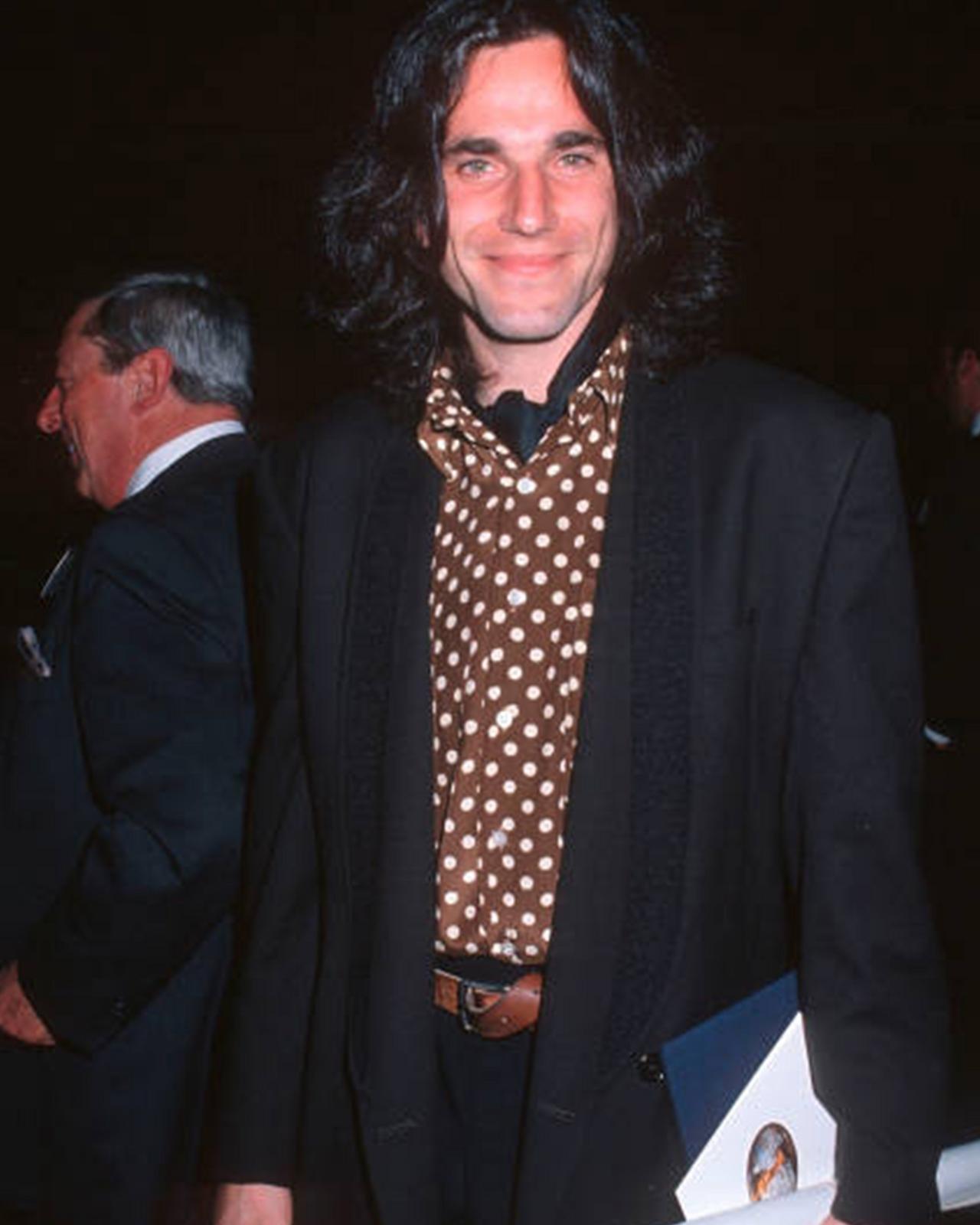 Daniel Day in a suit and tie holding a folder