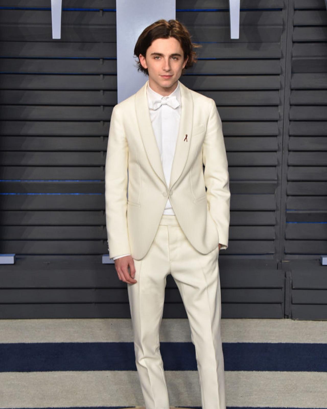 Timothée Chalamet in a white suit standing on a blue carpet