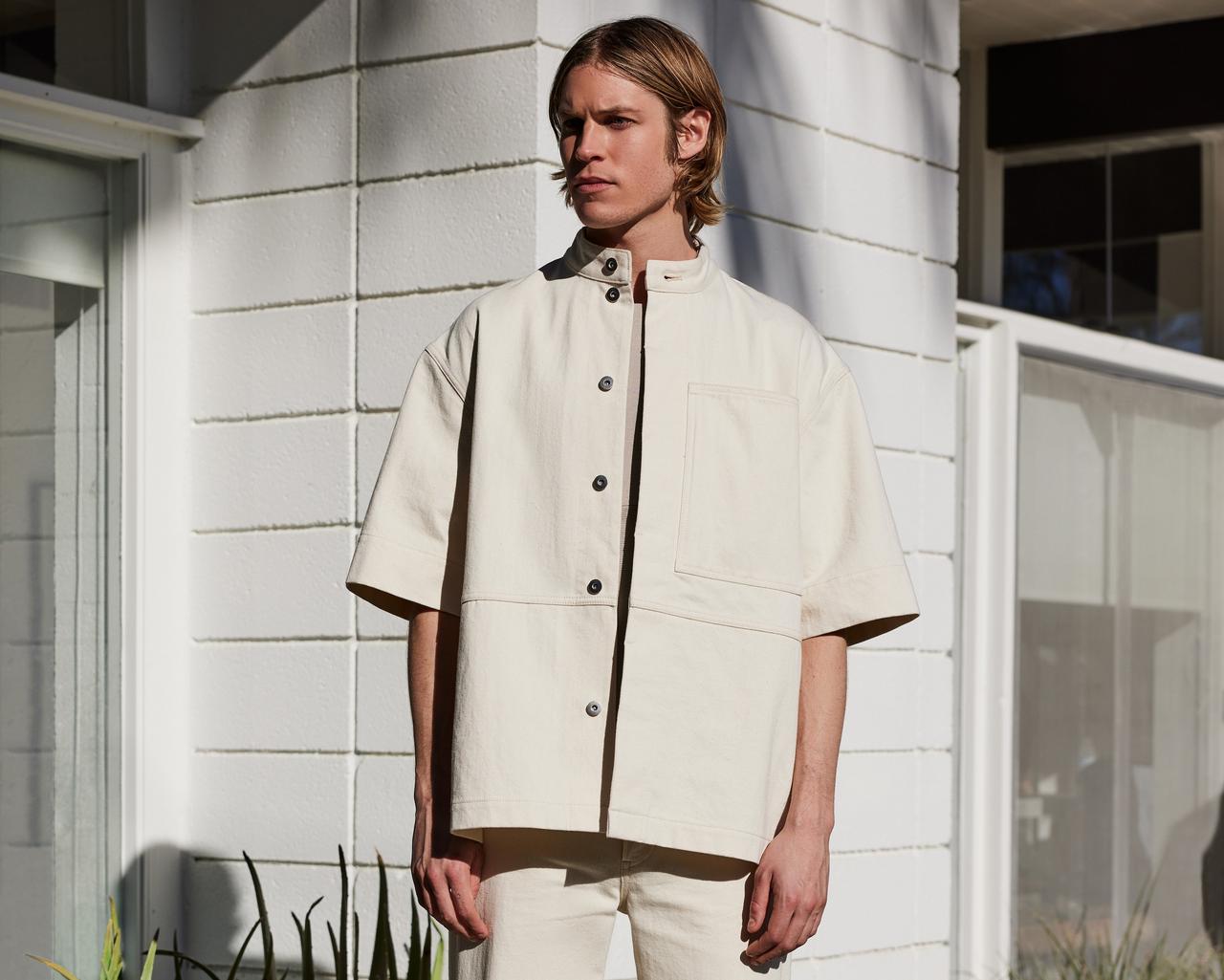 a man in a cream button up shirt standing in front of a house