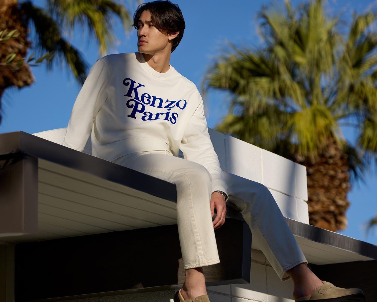a man sitting on top of a building with a white kenzo sweatshirt