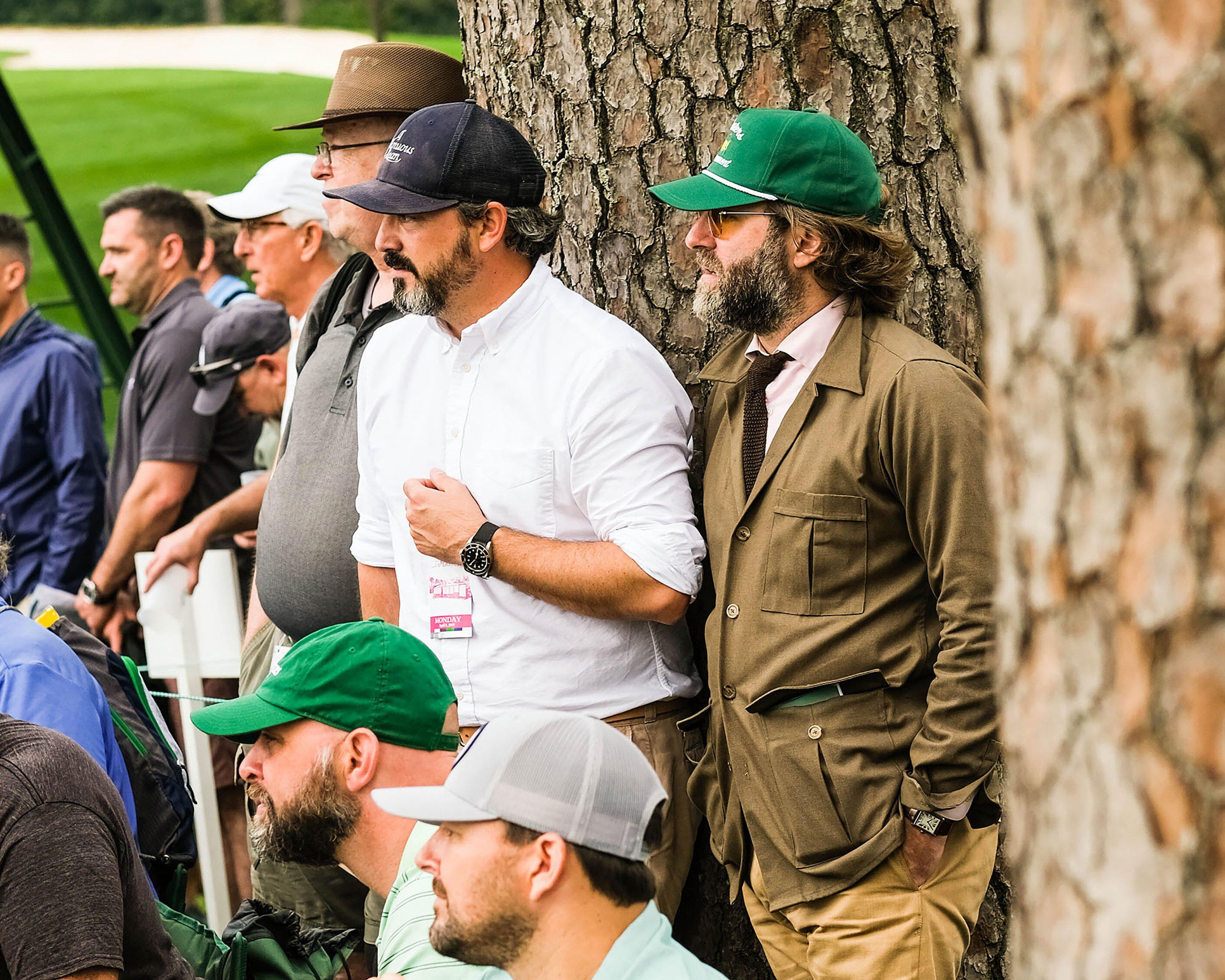 Two men leaning against a tree at the Masters