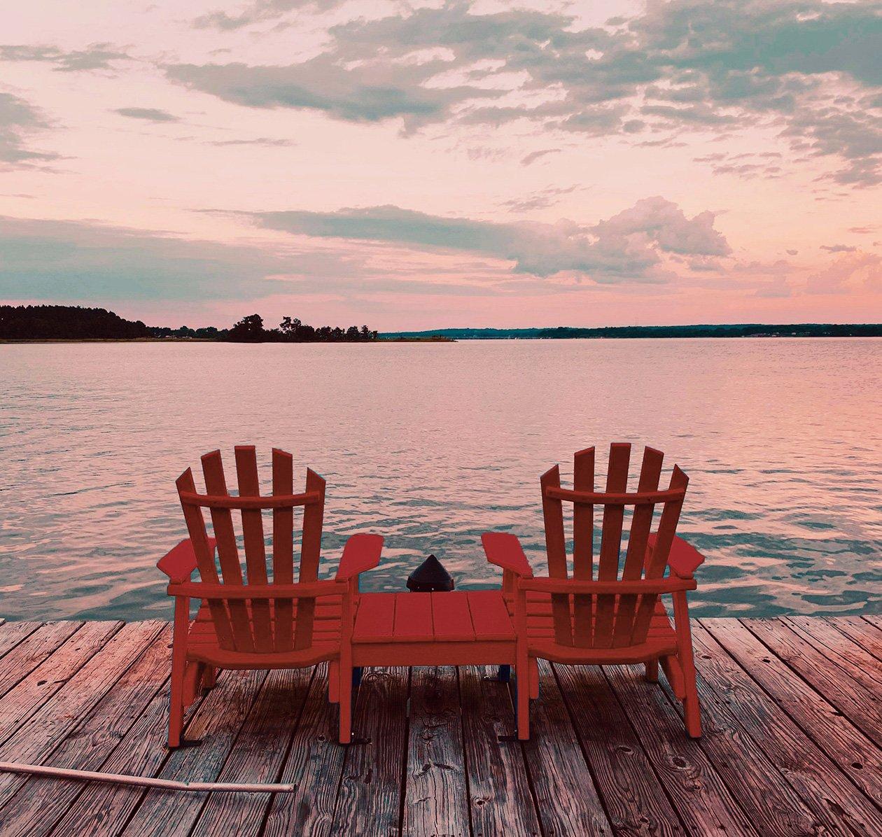two classic cottage chairs on a wodden dock facing lake in the sunset