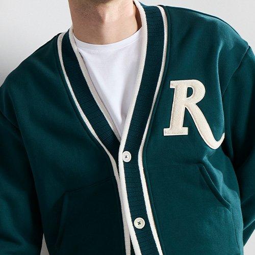 A man in a Rhude green sweater and black pants posing for a picture