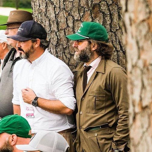 A group of men in hats and suits standing next to a tree at the Masters