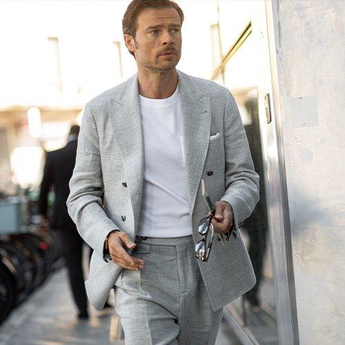 man in matching suit walking in the city holding glasses