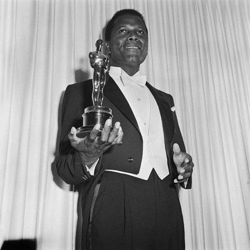 A black and white photo of a man in a tuxedo holding an oscar