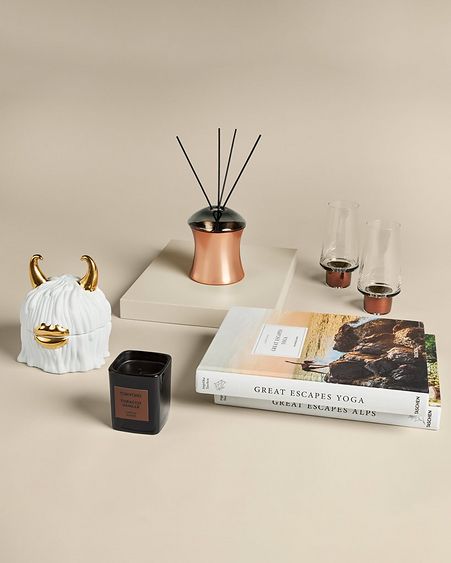 Collection of stylish home goods including scented candle, coffee table books, fragrance diffusers, and more