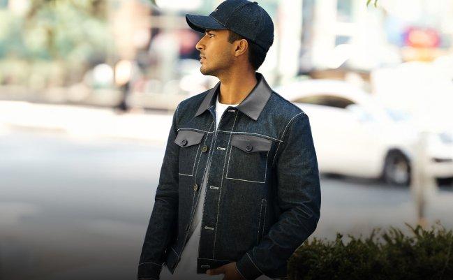 Man wearing a dark denim jacket with a matching cap, layered over a white shirt and dark jeans, standing outdoors