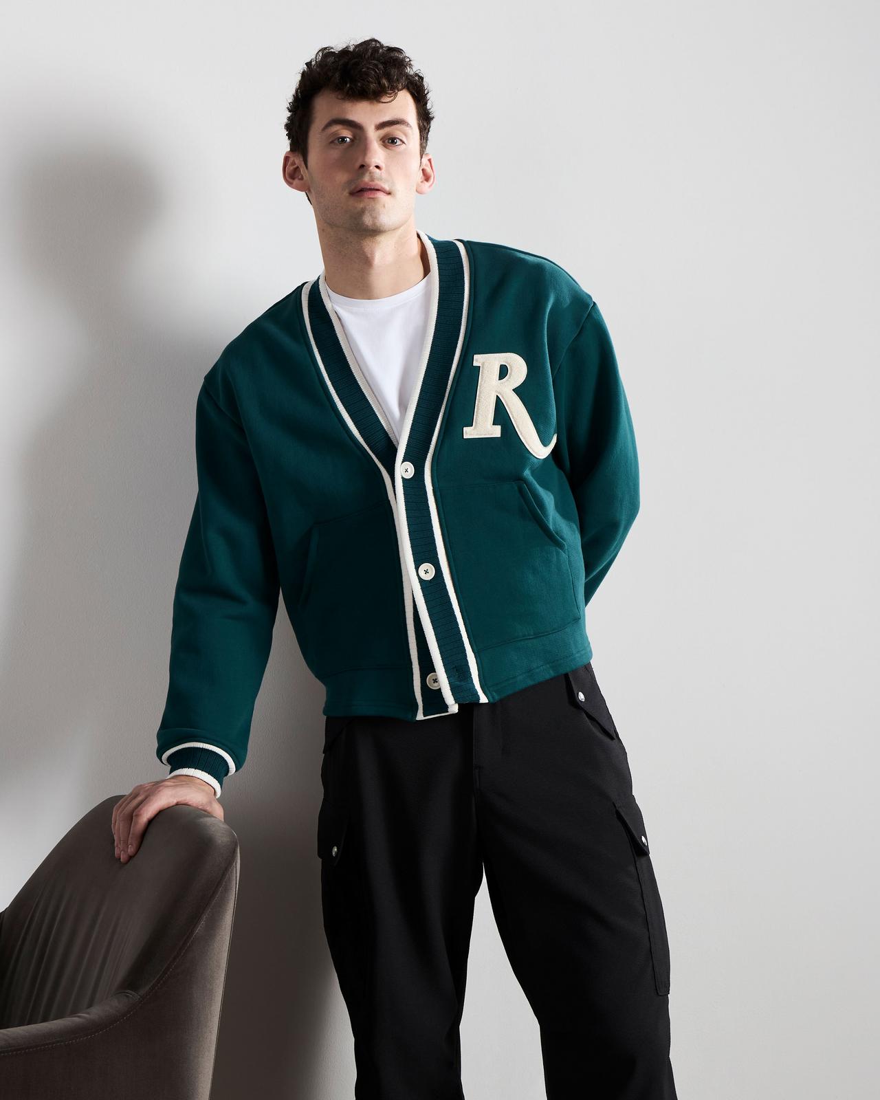 a man leaning against a chair in a green cardigan
