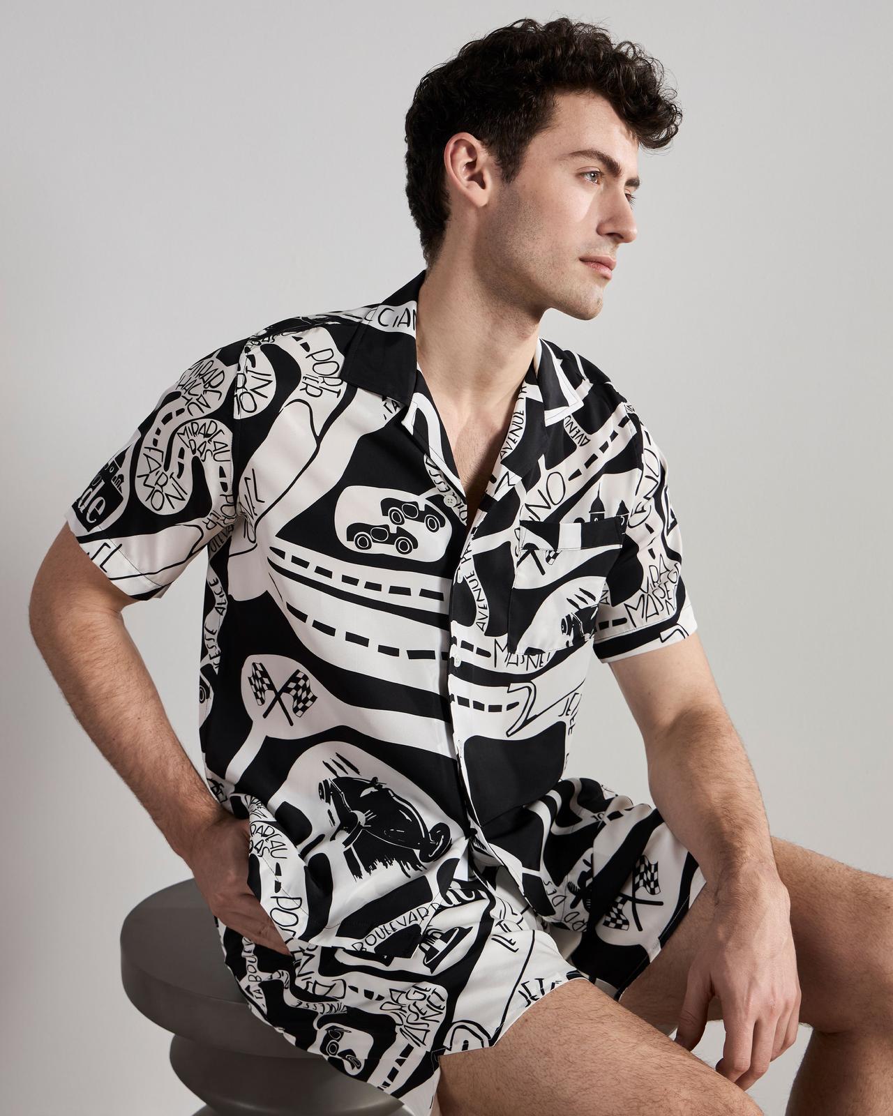 a man in a black and white patterned shirt and matching shorts sitting