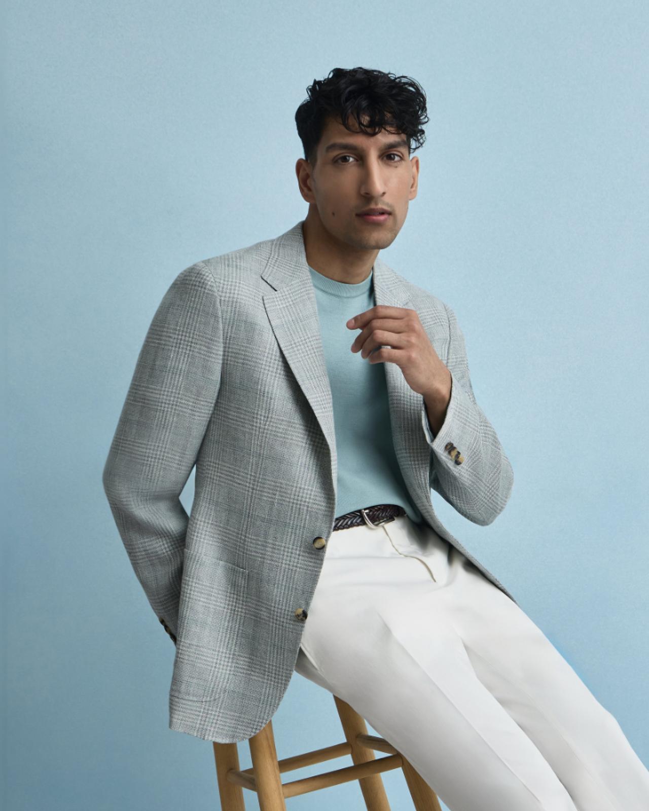 A model wearing a light blue grey sport jacket, turquoise shirt, styled with white pants and a black belt