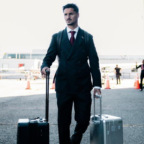 A man wearing a black suit holding his luggage at the airport