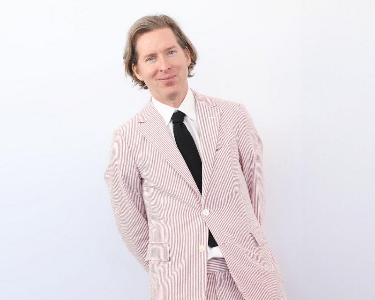 Wes Anderson wearing a light pink pinstriped suit with a black tie