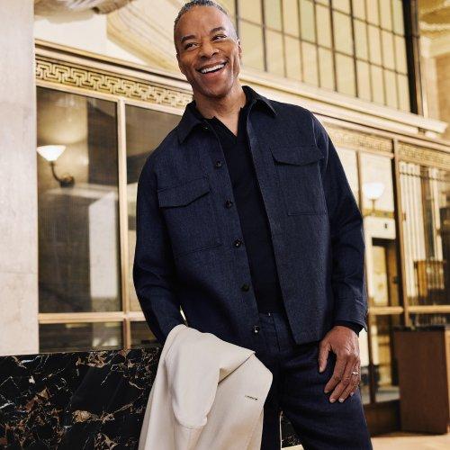 Un homme portant un polo rouge bordeaux, un pantalon blanc cassé et une ceinture brune