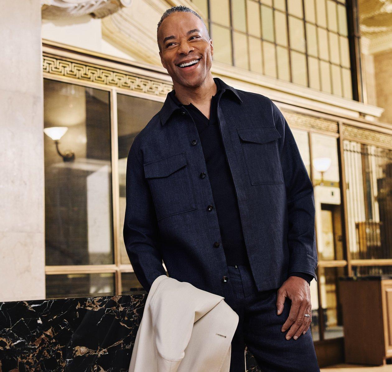 A man wearing a wine-red polo t-shirt with off-white pants and brown belt