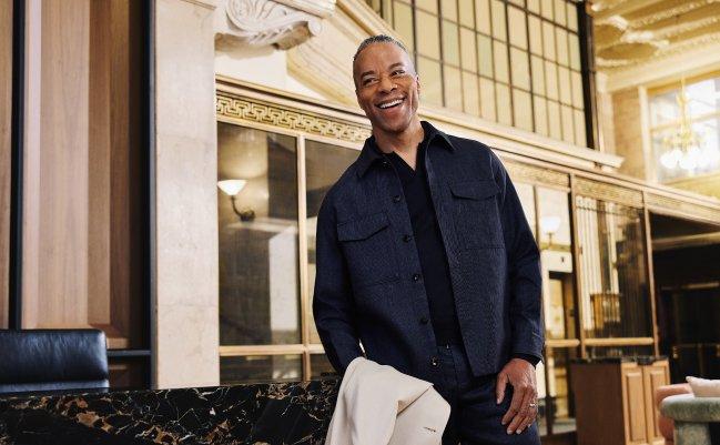 A man wearing a wine-red polo t-shirt with off-white pants and brown belt
