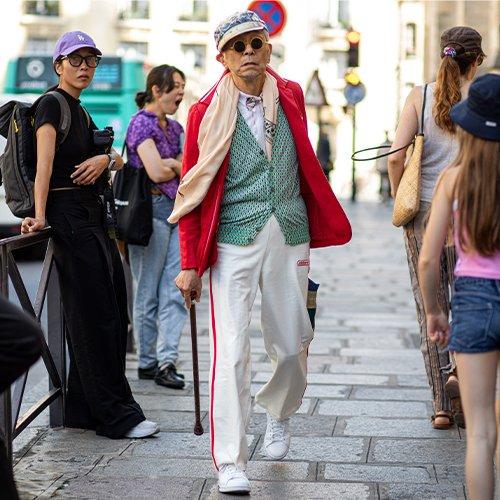 Un homme marchant dans la rue avec une veste de sport rouge, une canne et un chapeau
