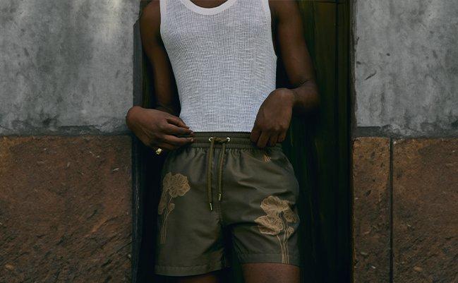 Model wearing a white tank and green swim trunks