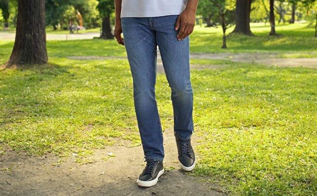 A man wearing blue jeans and black sneakers walking in a park
