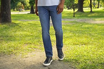 Image 15: A man wearing blue jeans and black sneakers walking in a park